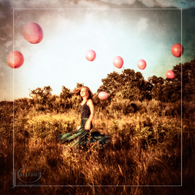 Fine art photograph of a young girl twirling in a field of wildflowers while pink balloons float above her head.